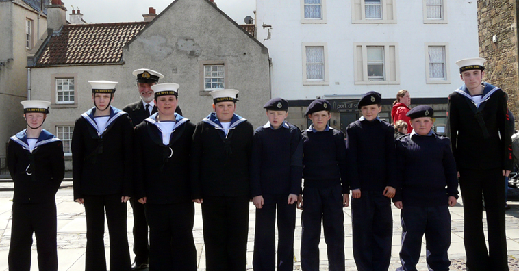 Nine young men in naval uniform stand in front of Newhaven village