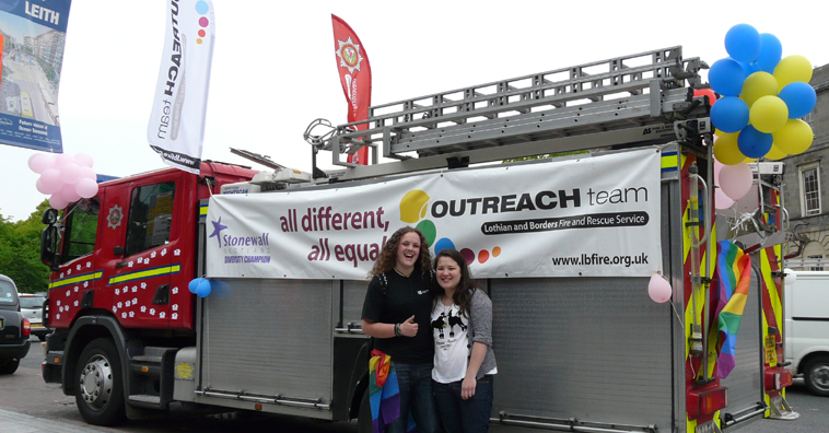 Two women standing in front of a fire engine sponsored by Stonewall and the Lothian & Borders Fire and Rescue Service Outreach Team with the slogan "all differentm all equal