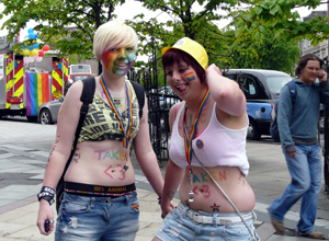 Two women with rainbow painted faces and the word TAKEN painted on their bellies