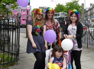 Three women in rainbow hats with a little girl in a buggy