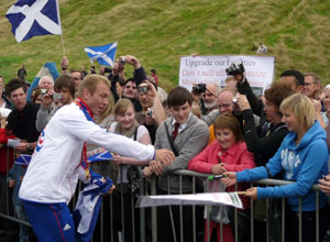 Chris Hoy reaching for a pen with the grass of Arthur's Seat in view